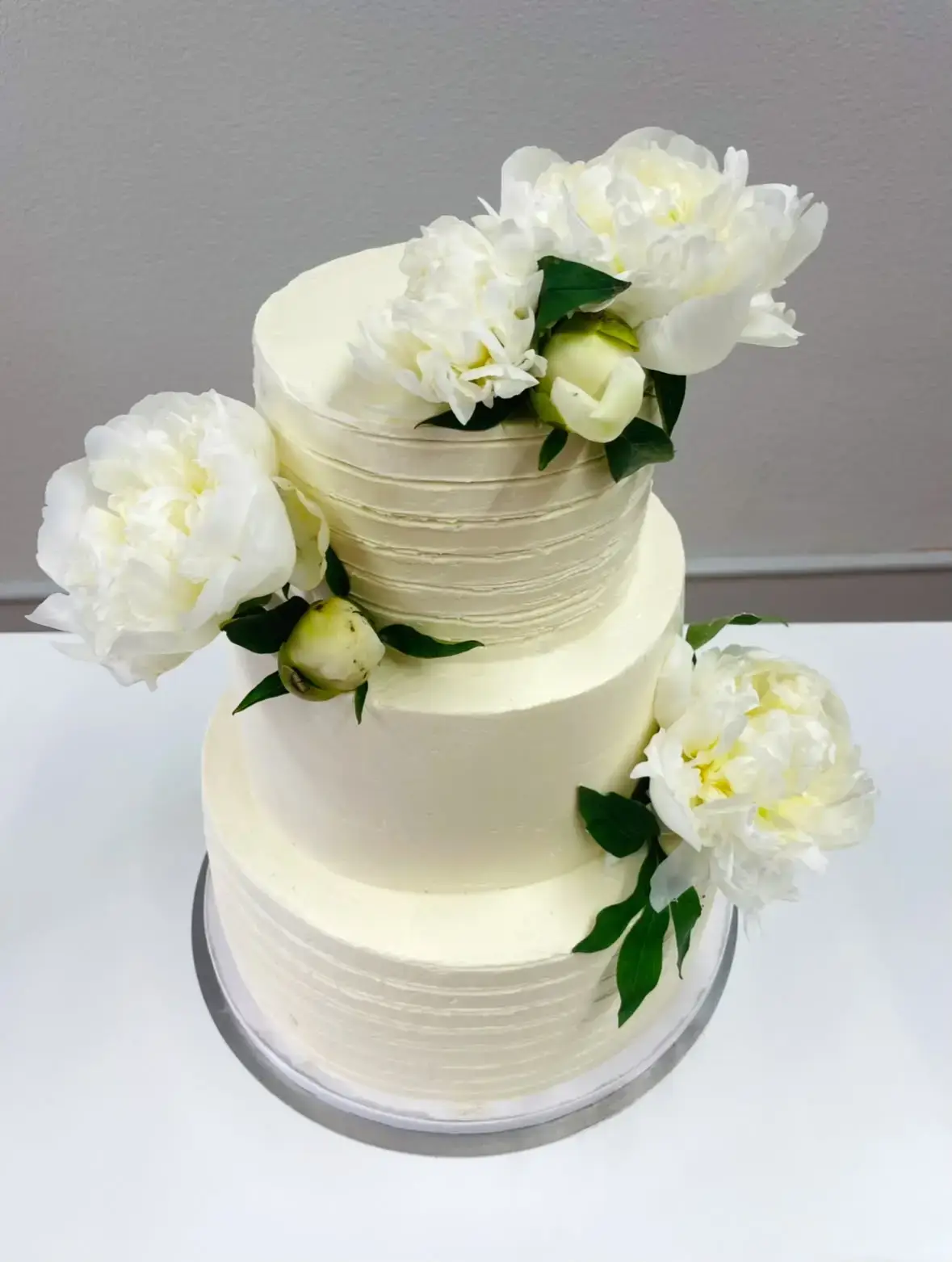 Dreistöckige weisse Hochzeitstorte mit grossen weissen Blüten und grünen Blättern.