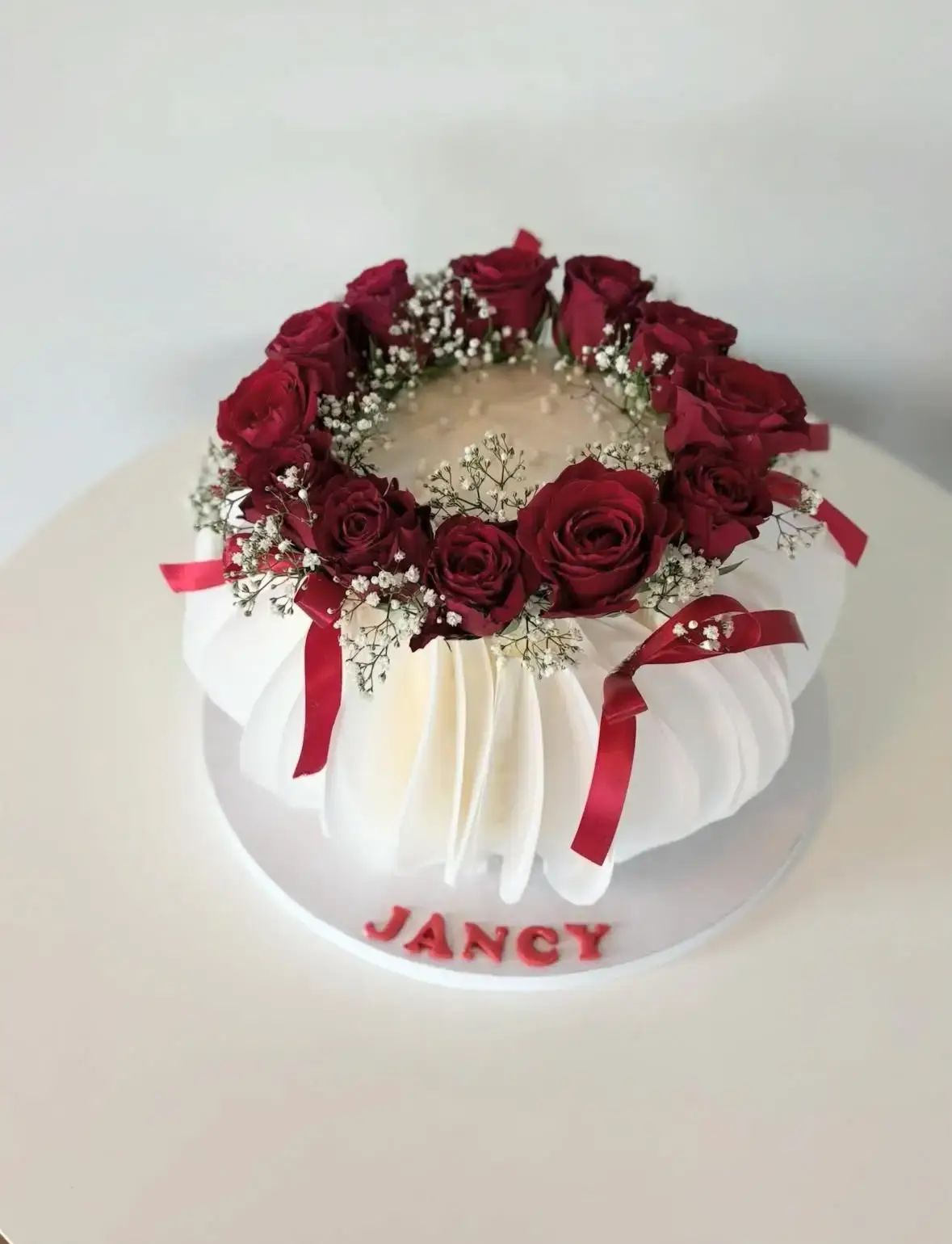 Weisse Torte mit einem Kranz aus roten Rosen, feinen weissen Blüten und roten Schleifen.