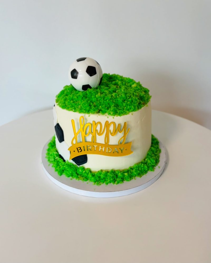 Weisse Geburtstagstorte mit Fussball, grünem Rasen und goldenem Happy-Birthday-Schriftzug.