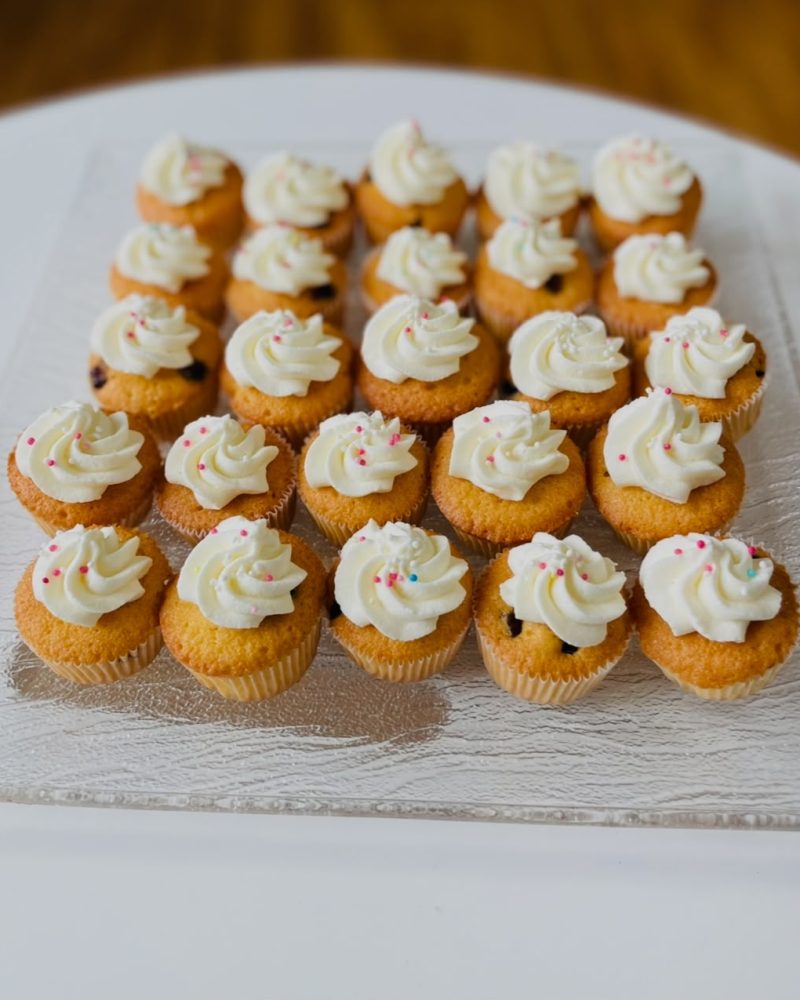 Mini Cupcakes mit heller Creme und bunten Zuckerperlen auf einer silbernen Platte.