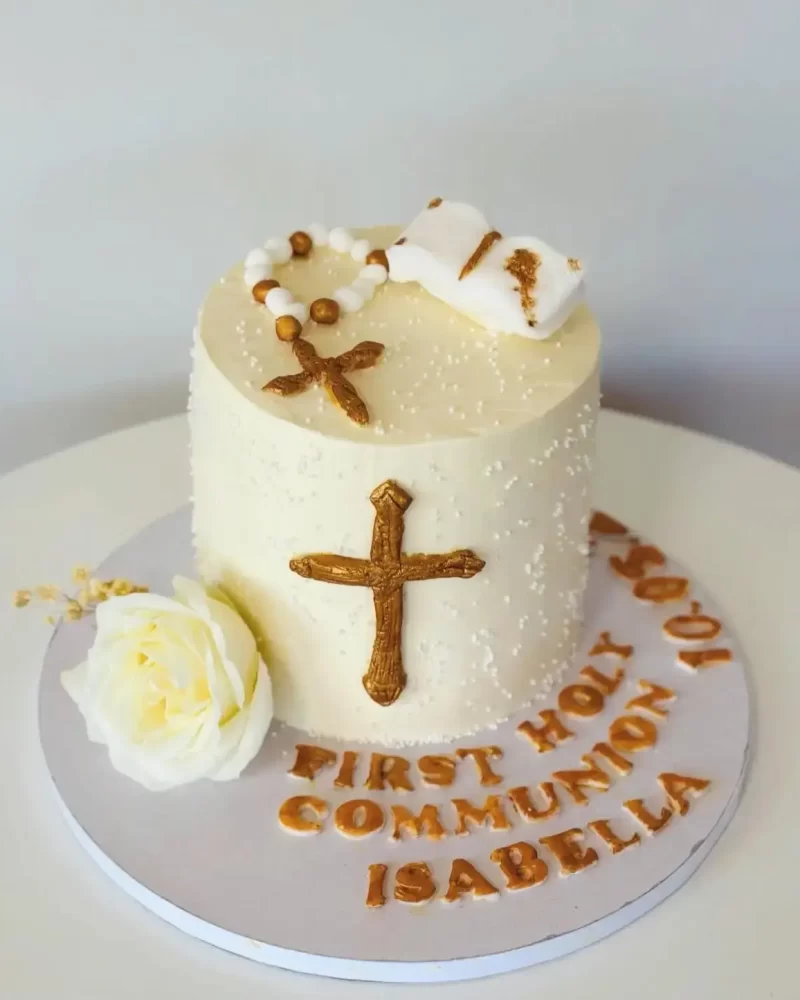 Weisse Kommuniontorte mit goldenem Kreuz, Rosenkranz, kleinem Buch und einer weissen Rose.