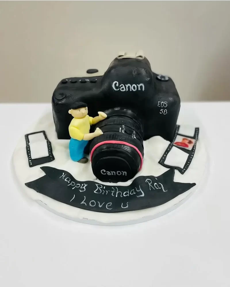 Motivtorte in Form einer schwarzen Canon Kamera mit kleiner Figur und Filmstreifen.