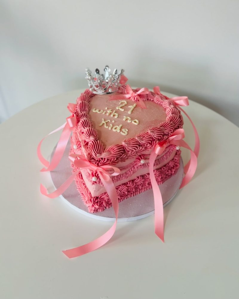 Rosa Herztorte mit Krone, Schleifen und der Aufschrift 21 with no Kids.